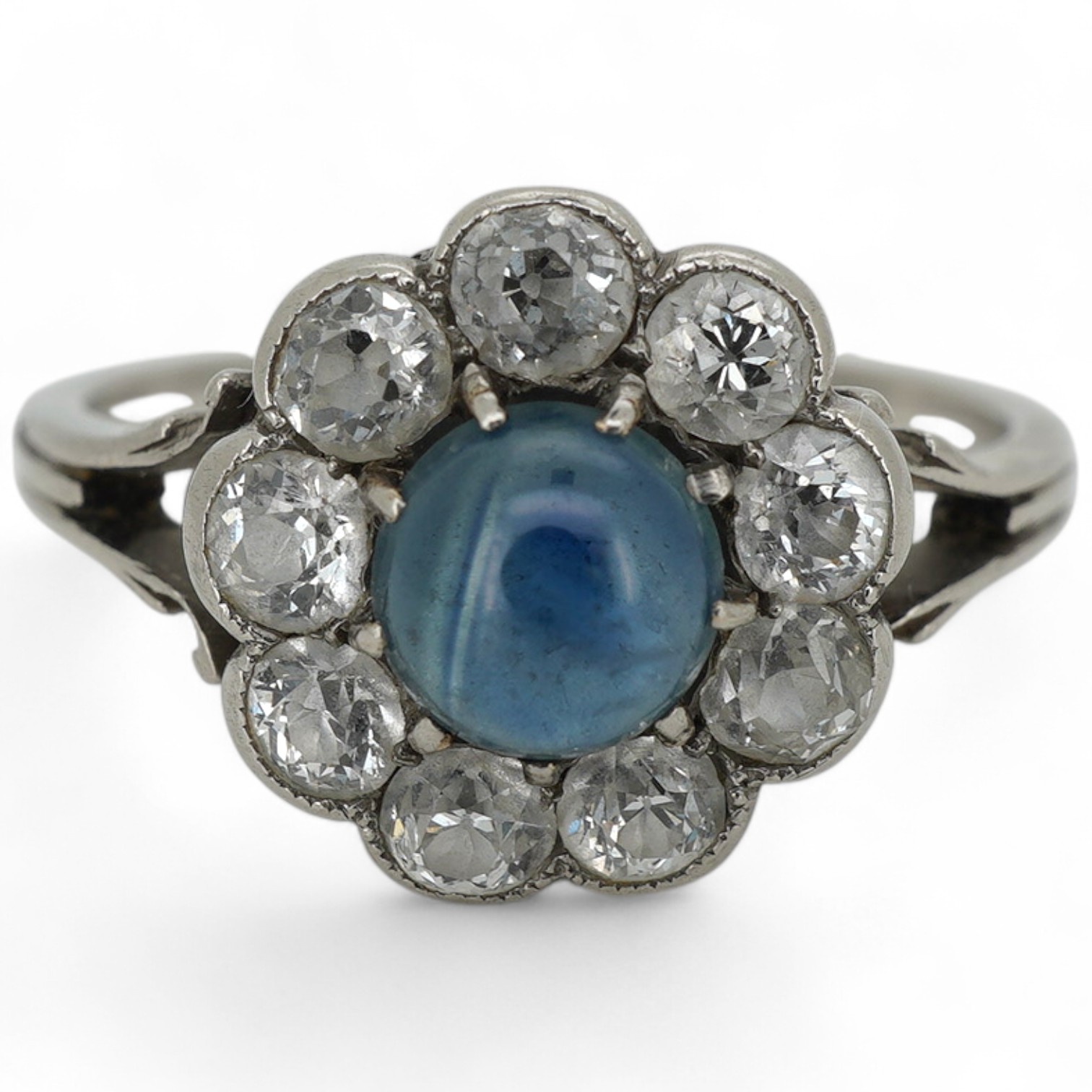 A sapphire and diamond cluster ring, early 20th century, set with a cabochon sapphire measuring approximately 5 x 5 x 3mm, within a border of circular-cut diamonds totalling approximately 0.90 carats, size M, gross weigh